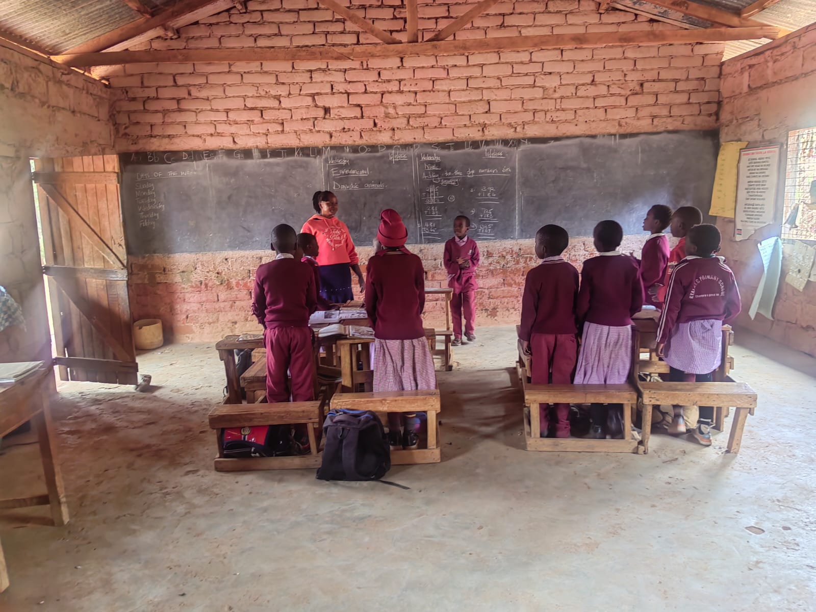 Learners in red uniforms facing the classroom chalkboard